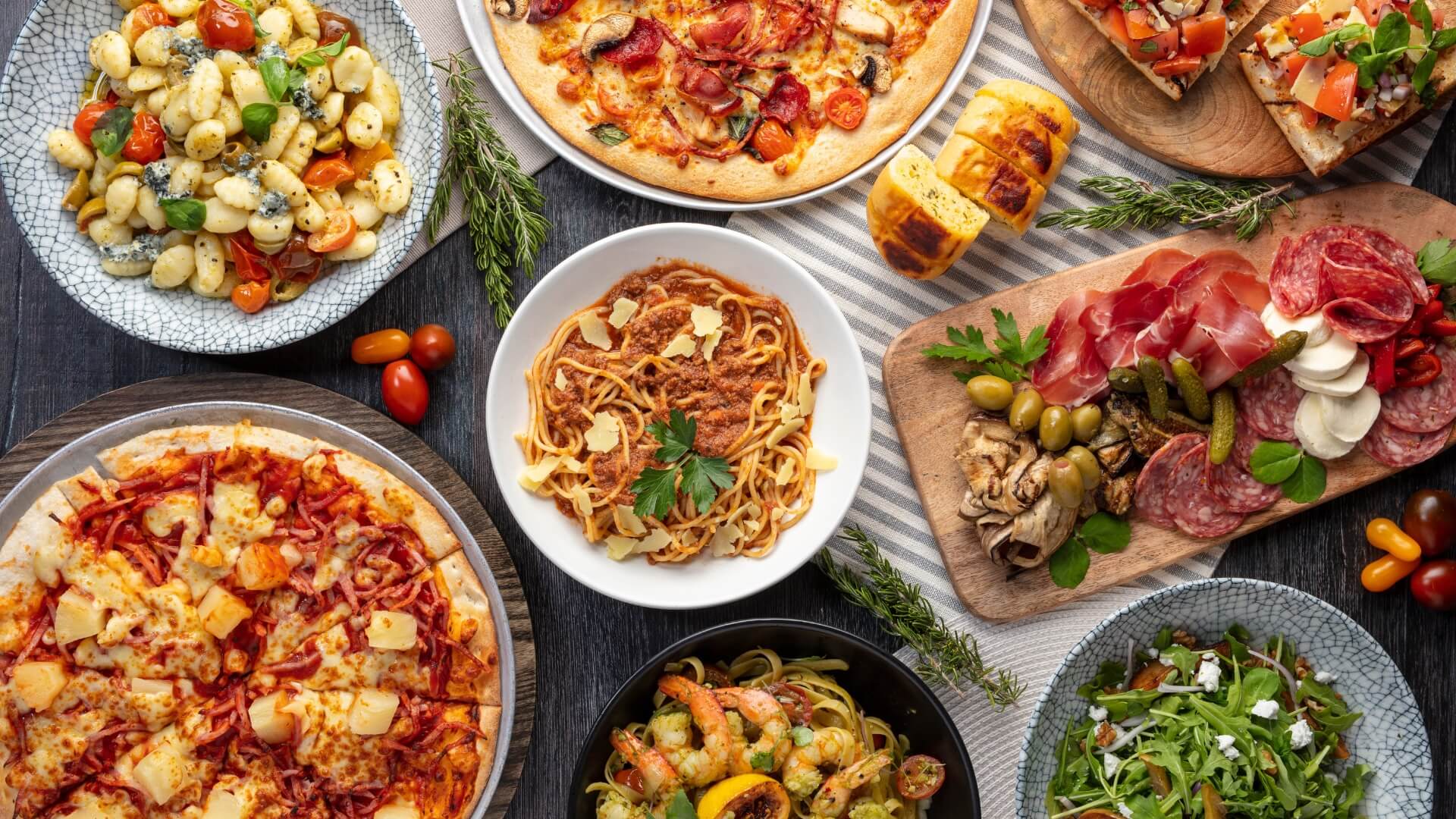 A table with assorted Italian dishes, including pasta, pizza, bruschetta, salad, and a charcuterie platter, from Melrose Italian at Sea World Resort.