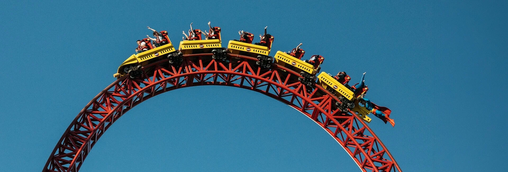 Riders on the Superman Escape roller coaster at Movie World, travelling over a tall red steel track against a clear blue sky.