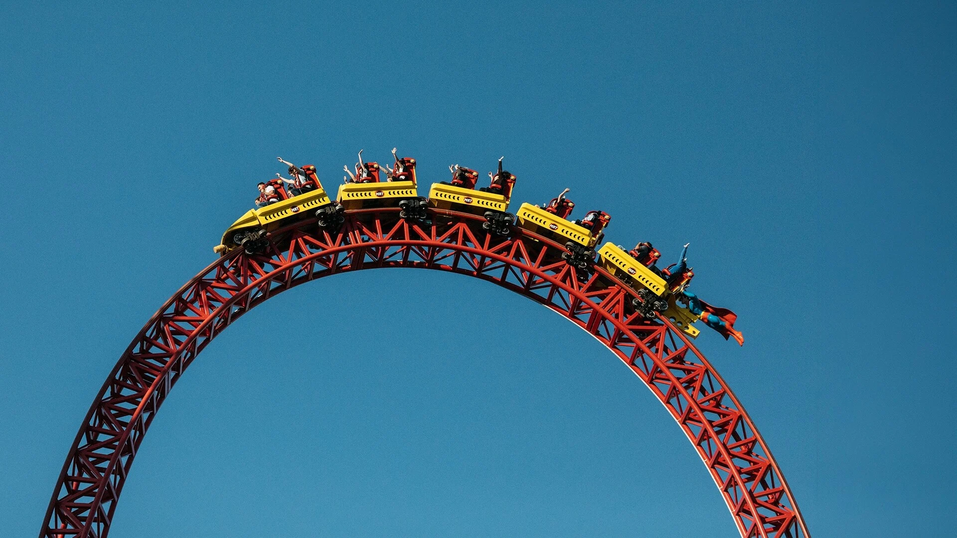 Riders on the Superman Escape roller coaster at Movie World, travelling over a tall red steel track against a clear blue sky.