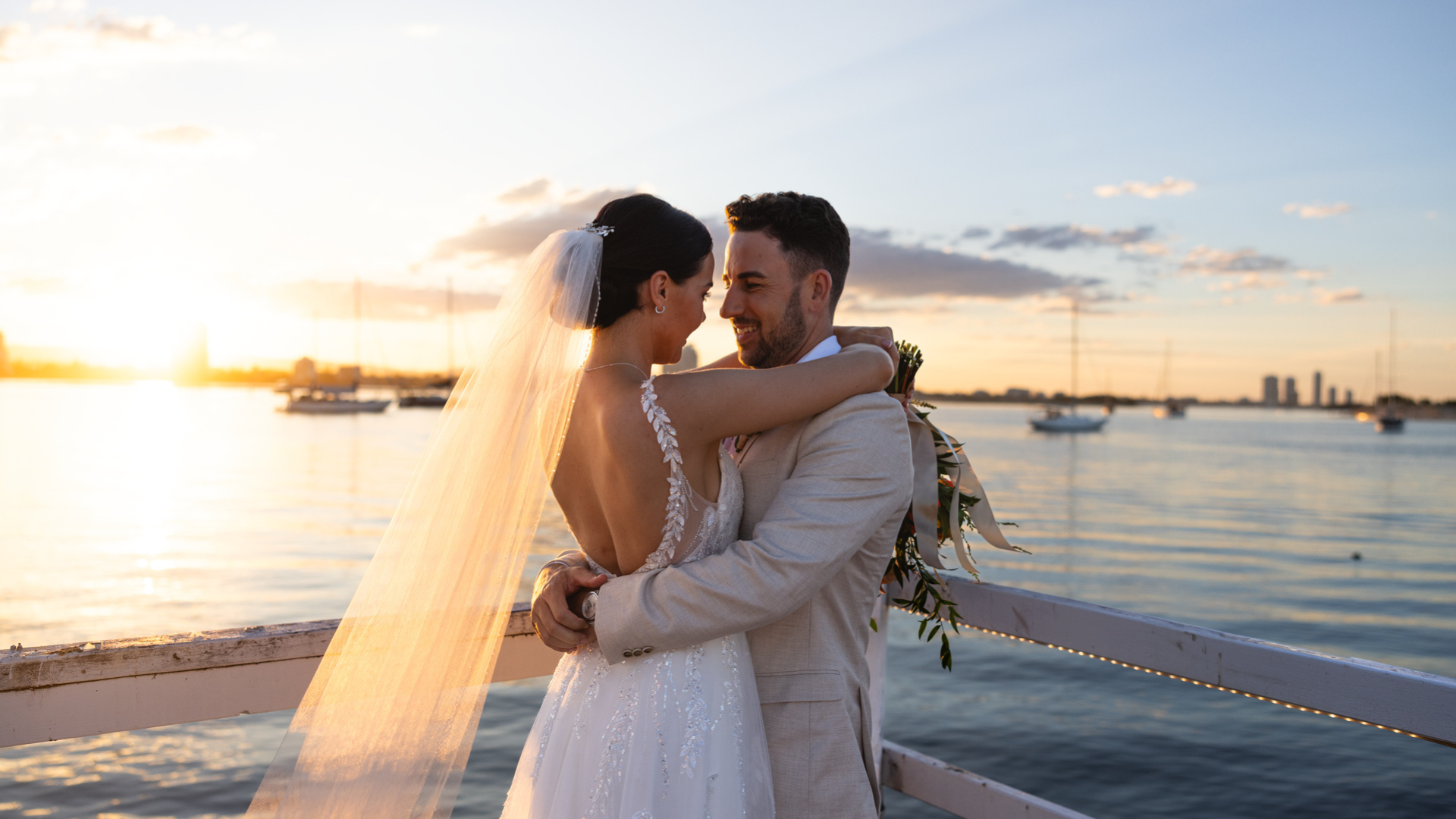 Bride and groom embracing on a pier at The Boatshed, Sea World Resort, at sunset with boats and the Broadwater in the background. Weddings