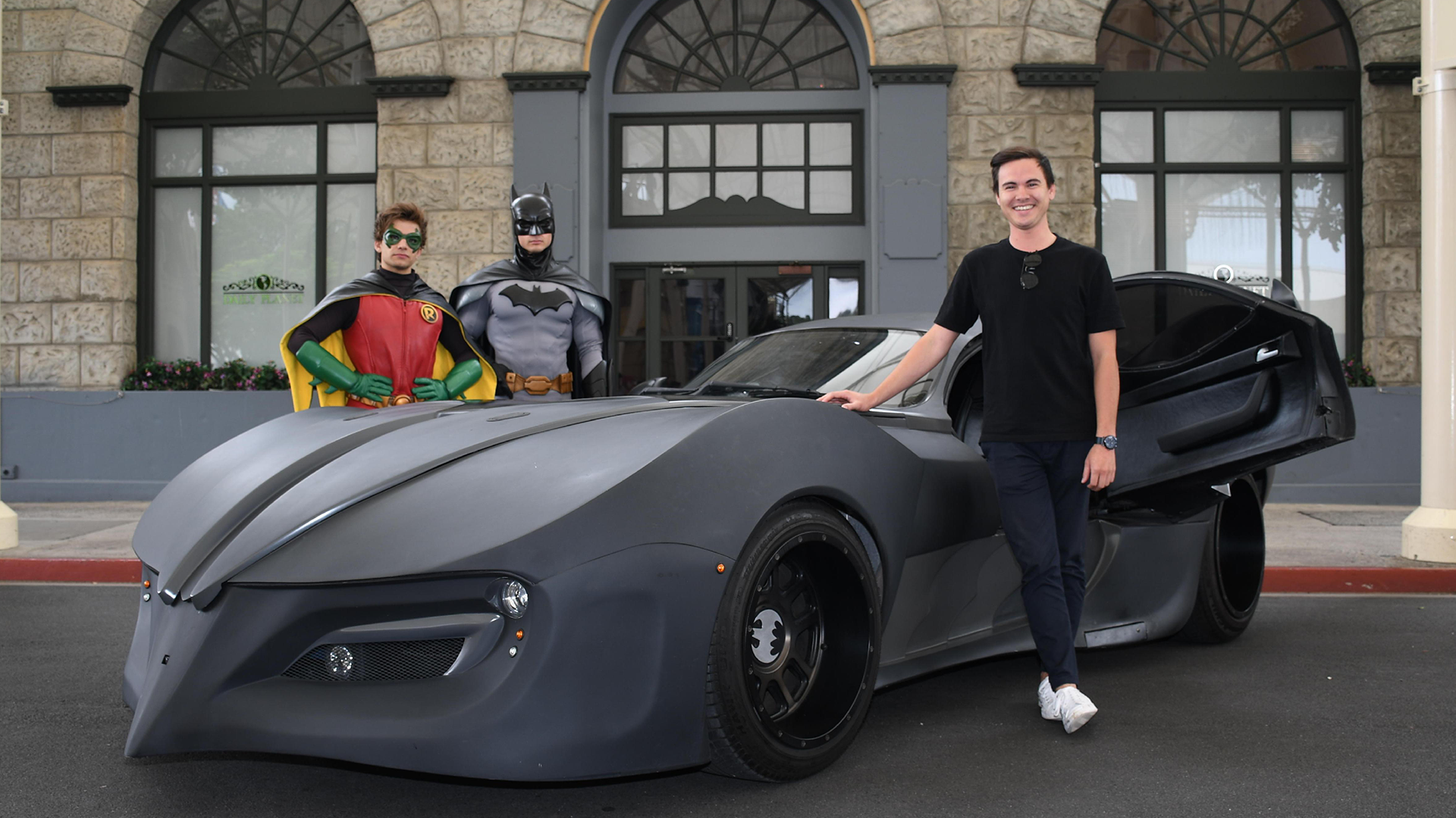 A person posing proudly in front of the Batmobile on Main Street at Warner Bros. Movie World