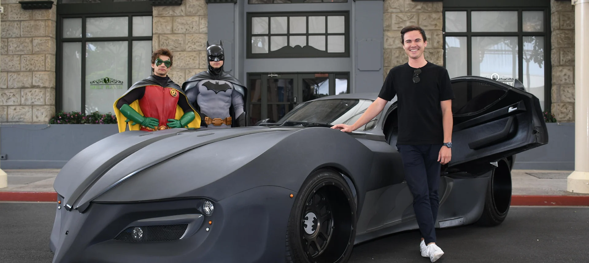 A person posing proudly in front of the Batmobile on Main Street at Warner Bros. Movie World