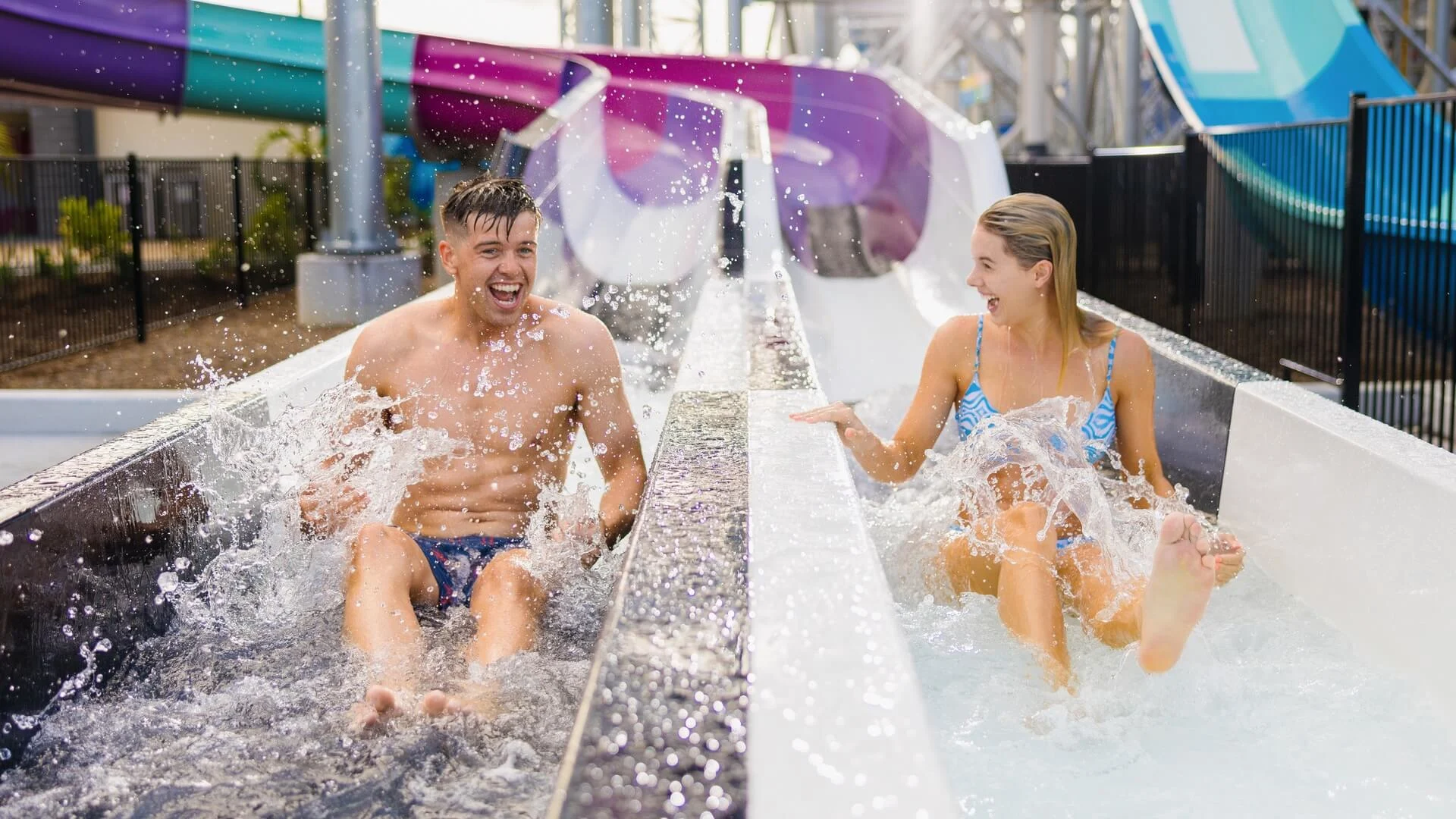 Friends splashing and laughing as they race side by side down the Super Ripper water slides at Wet’n’Wild.