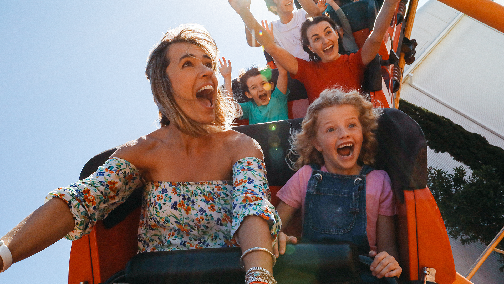 A group of cheerful people, including children and adults, enjoying a roller coaster ride on a bright, sunny day.