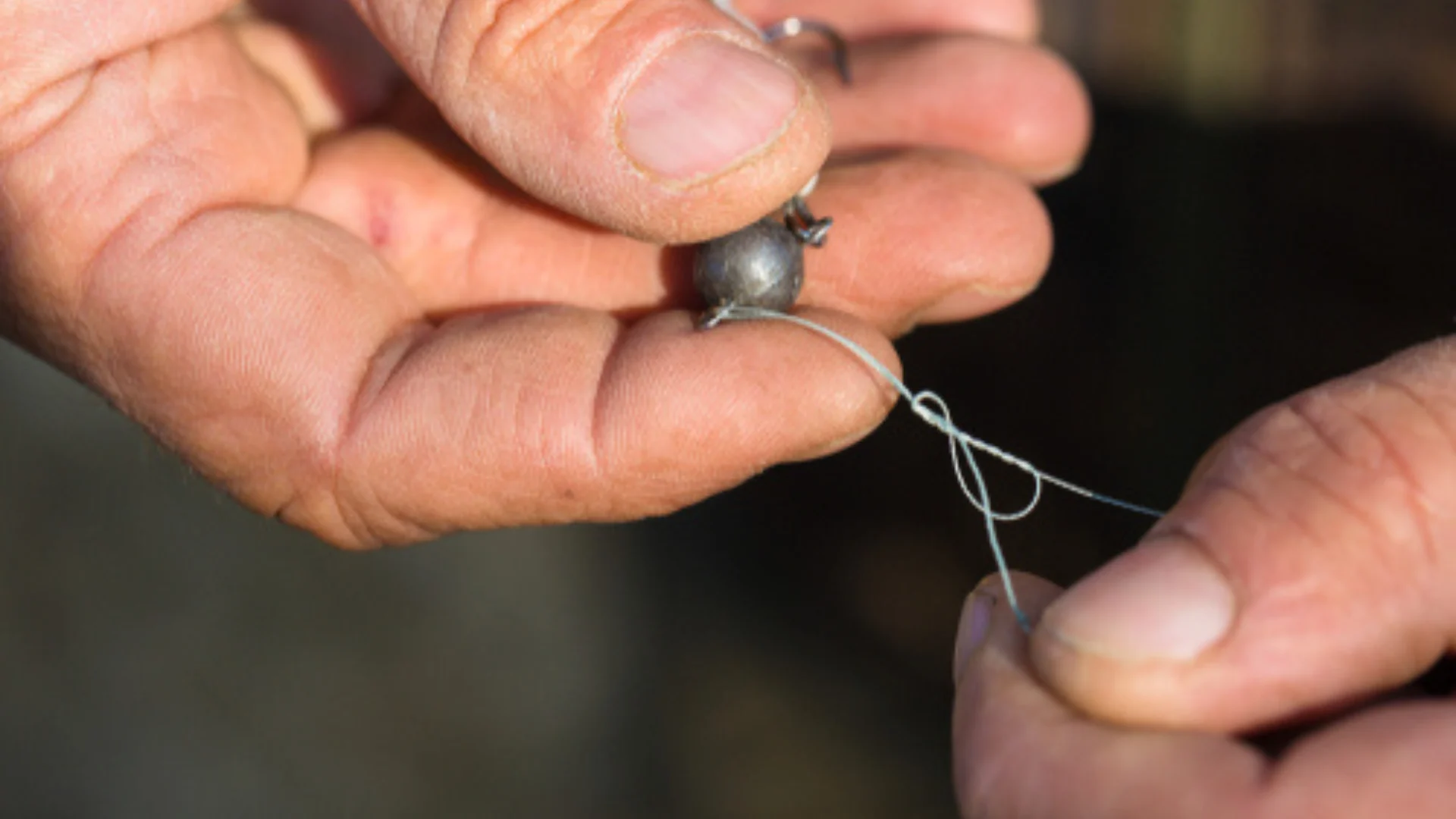 Close-up of hands tying fishing line to a round fishing weight, preparing fishing tackle.
