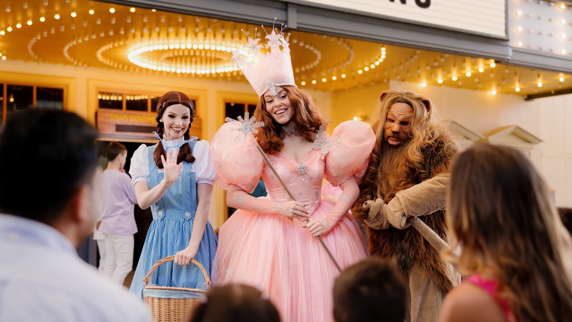 Dorothy, Glinda the Good Witch, and the Cowardly Lion greeting families in front of a brightly lit theatre at Warner Bros. Movie World.