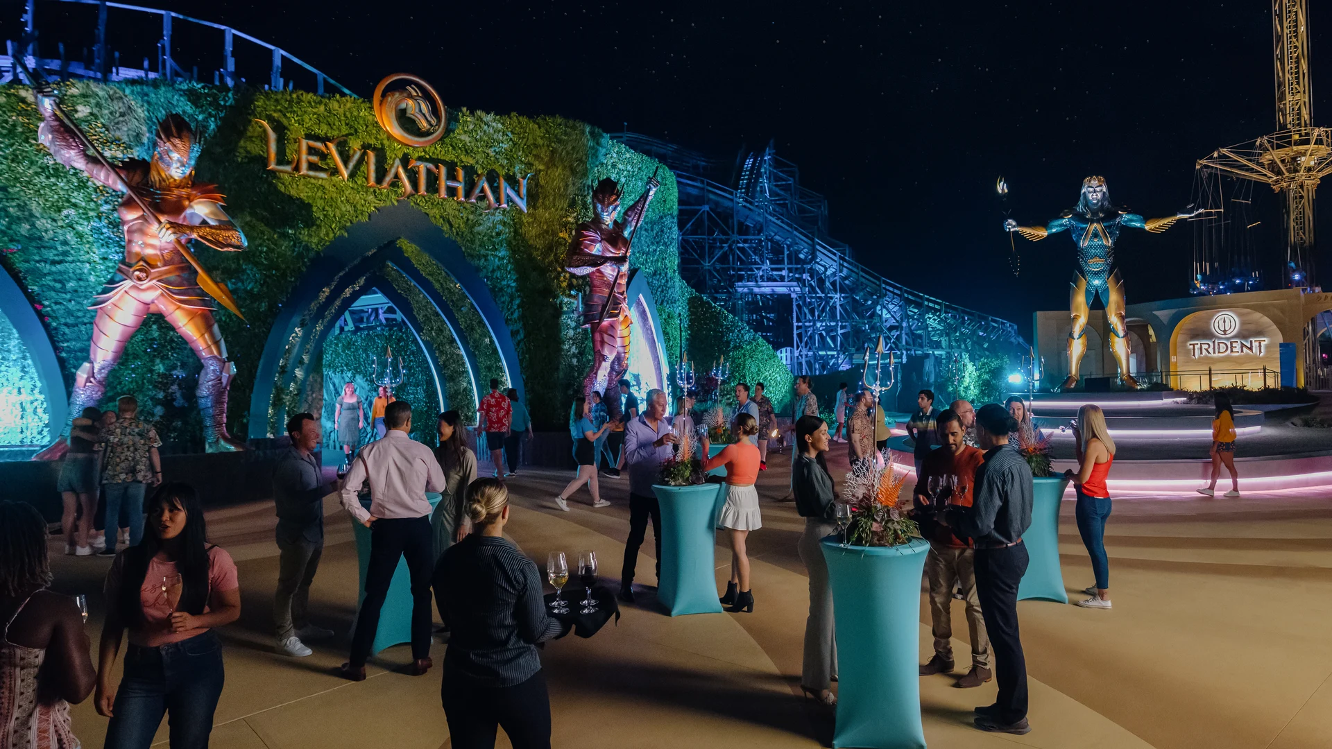 People gather at an outdoor evening event in front of a large "Leviathan" sign with illuminated statues and themed decorations.