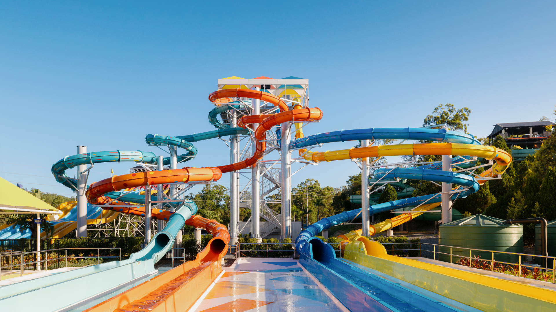 A large outdoor water park with multiple interconnected colorful slides twisting from a central tower down to several landing lanes.