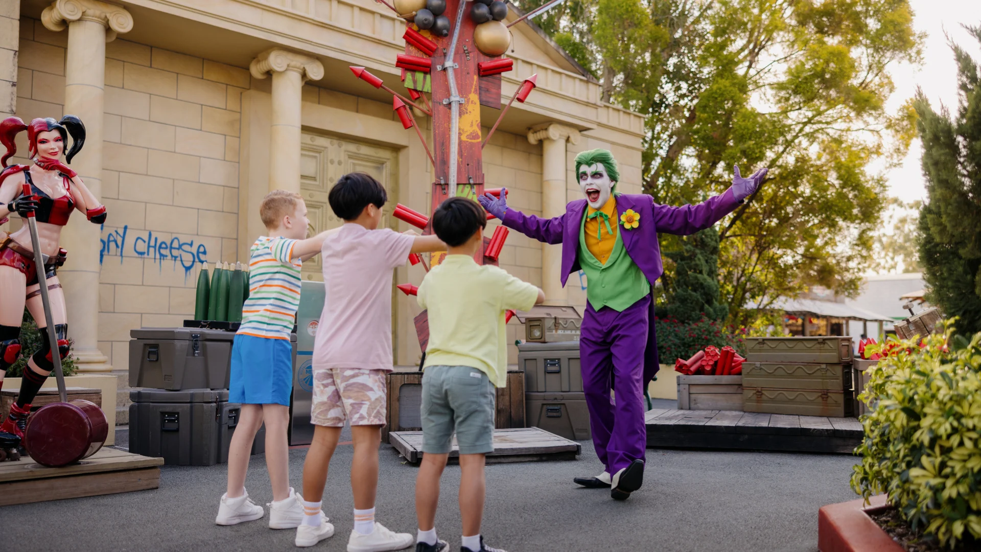The Joker smiling at 3 kids with arms raised in a playful pose at Warner Bros. Movie World
