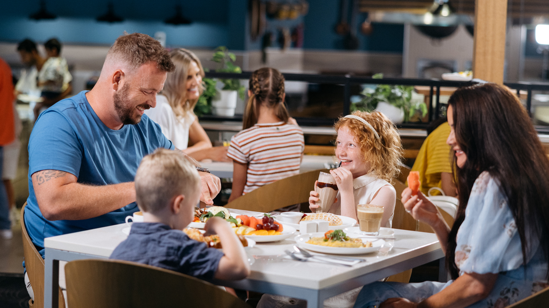 A smiling family of four enjoys a meal together at a restaurant, with plates of food and drinks on the table.
