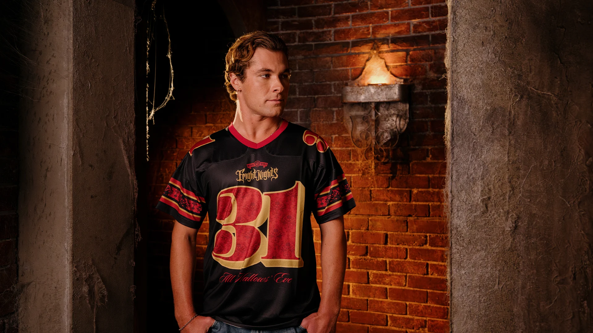 A young man wearing a black and red jersey with the number 31 stands in a dimly lit brick corridor, looking to the side with his hands in his pockets.