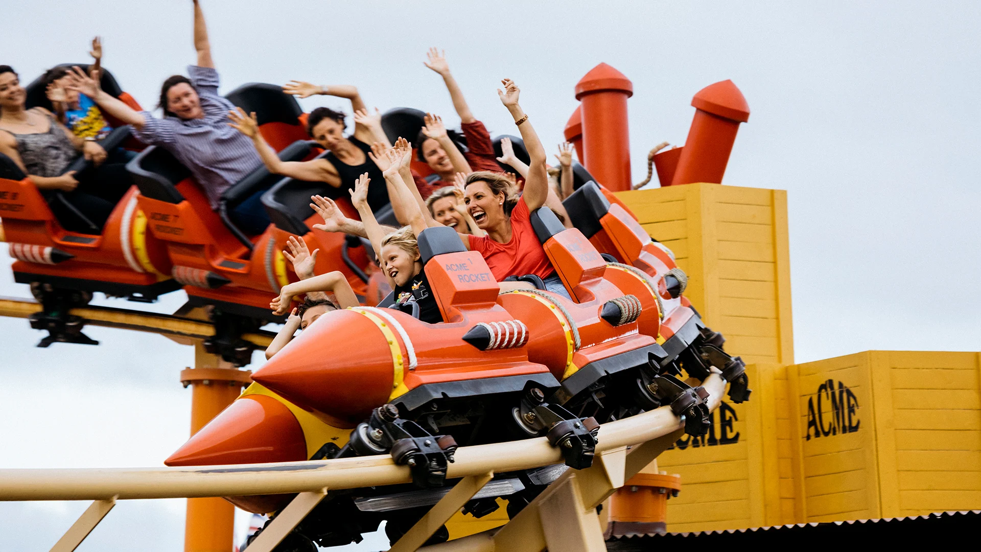 Families smiling and raising their hands in the air while riding the Road Runner Rollercoaster at Warner Bros. Movie World