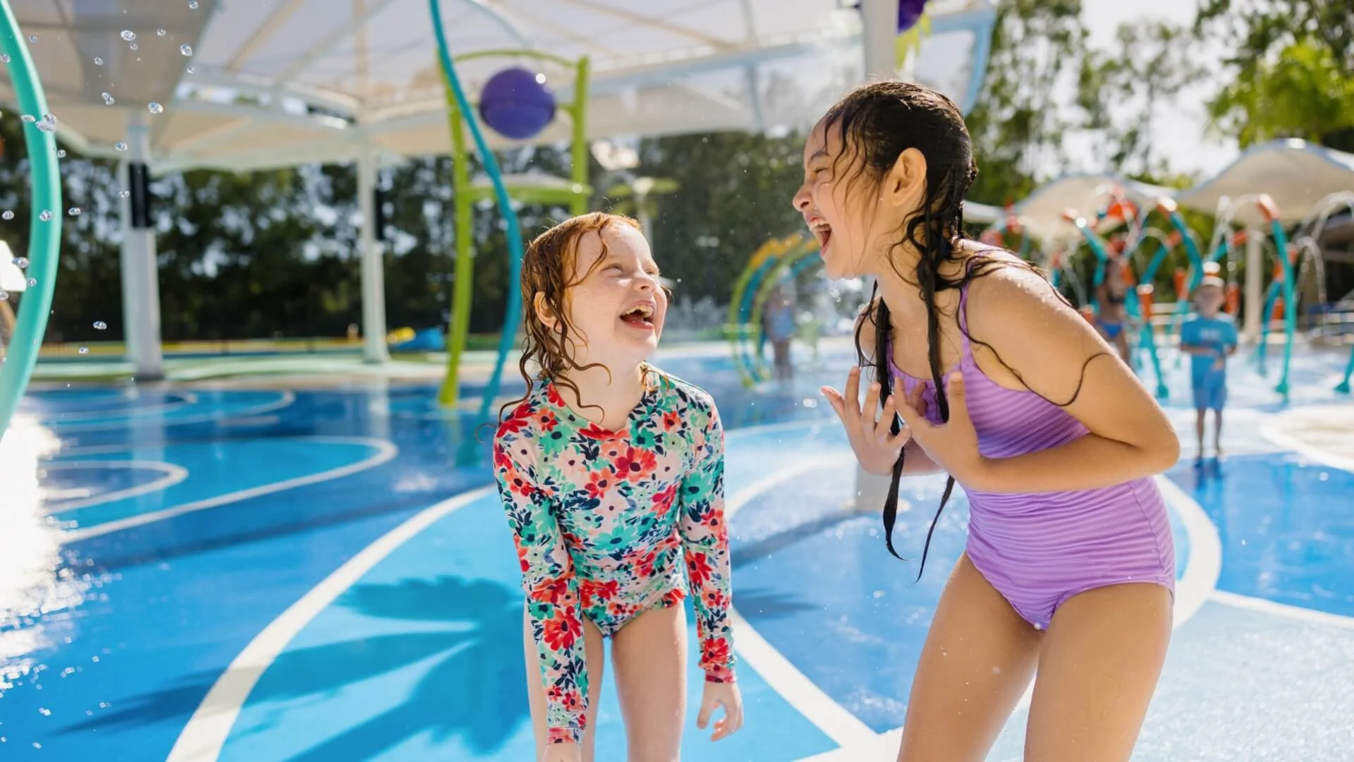 Two children laughing and playing in the H2Oasis splash park at Wet'n'Wild on the Gold Coast, surrounded by water features and bright sunlight.
