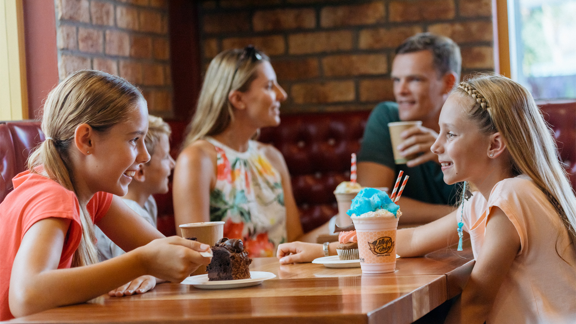 A family of five sits at a restaurant table, enjoying drinks and desserts while having a conversation.