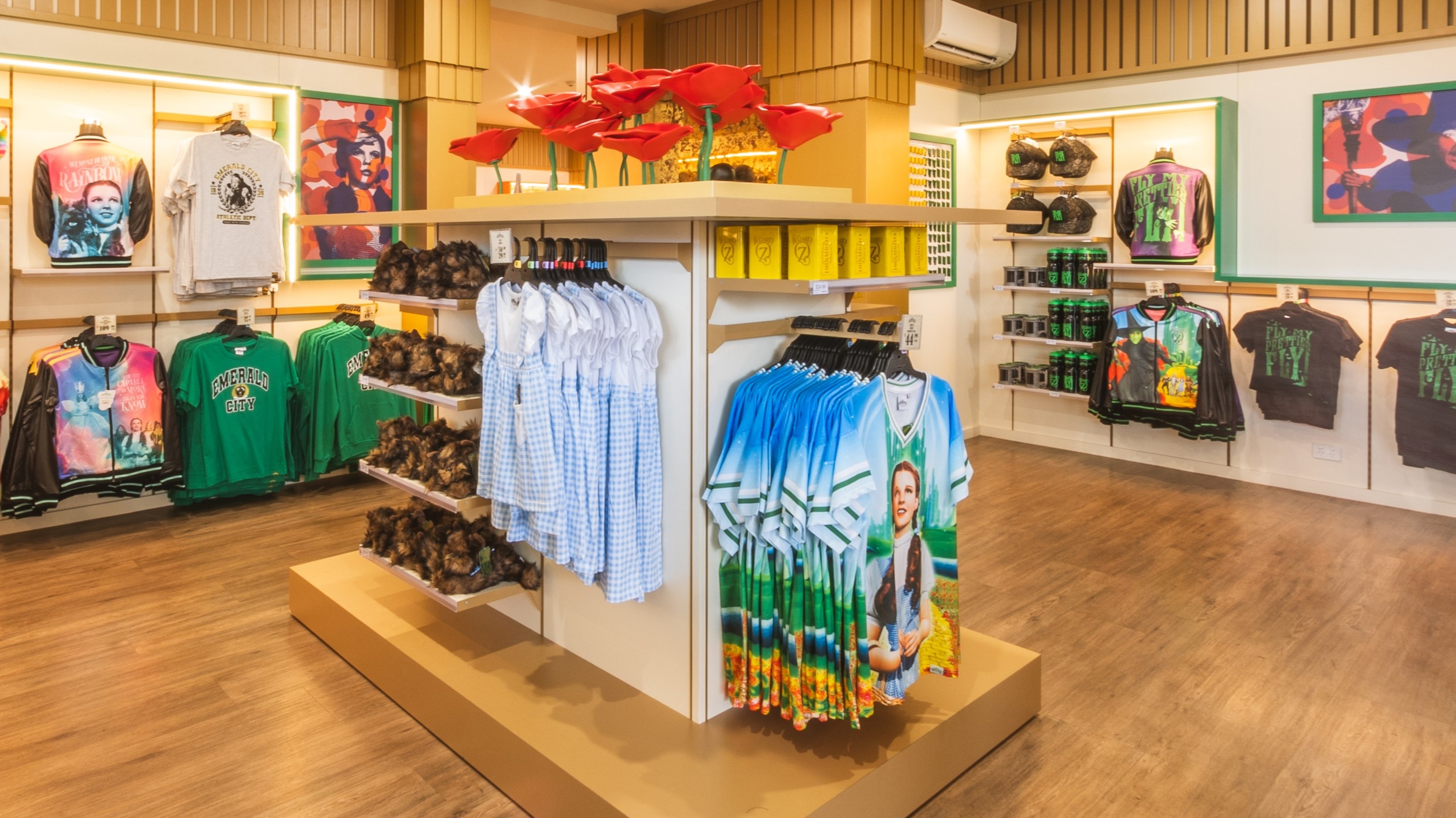 A retail store interior displaying various T-shirts, shirts, and merchandise on racks and shelves, with bright lighting and wooden flooring. WOZ