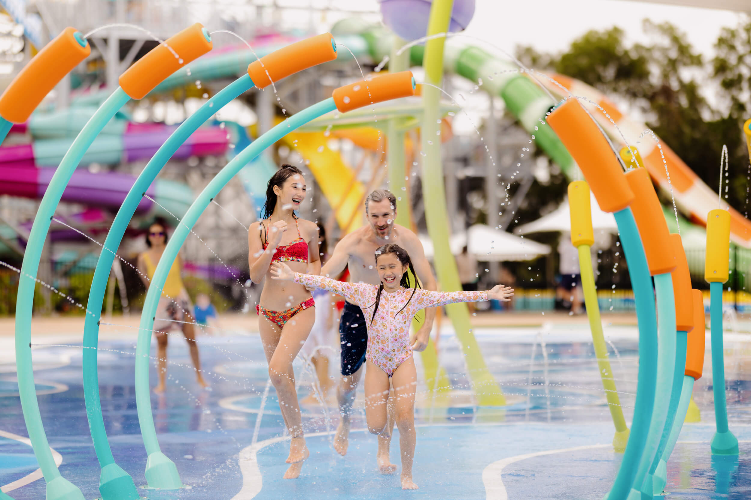 Family running and laughing through colourful water arches at the H2Oasis splash zone in Wet’n’Wild Gold Coast, surrounded by bright slides and playful water sprays