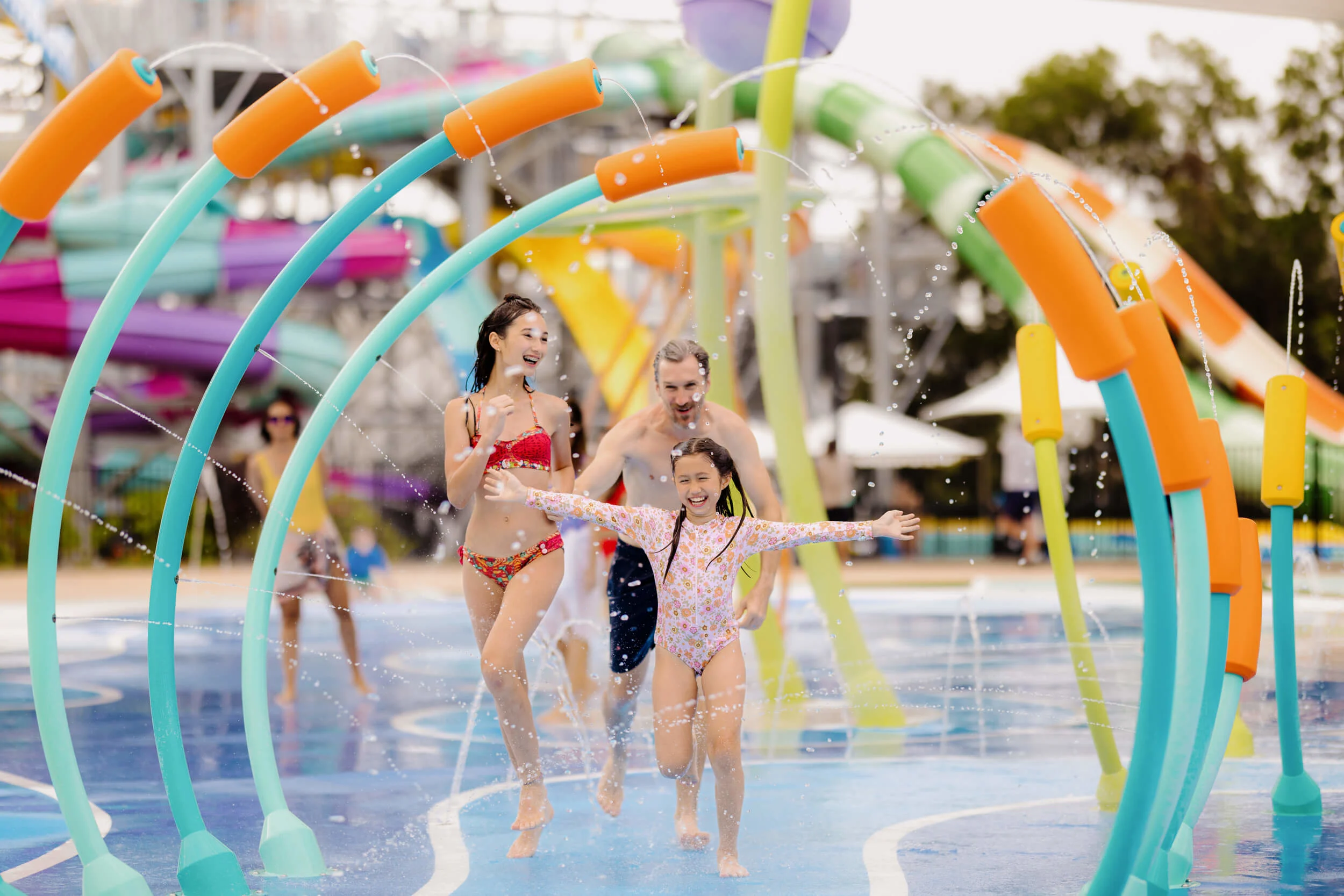 Family running and laughing through colourful water arches at the H2Oasis splash zone in Wet’n’Wild Gold Coast, surrounded by bright slides and playful water sprays