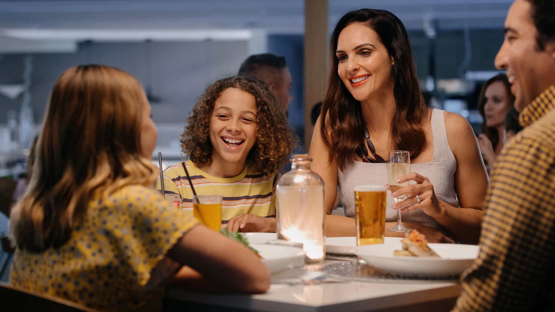 A group of four people sits at a table at Shoreline Restaurant, with drinks, laughing and enjoying each other's company in a warmly lit room.
