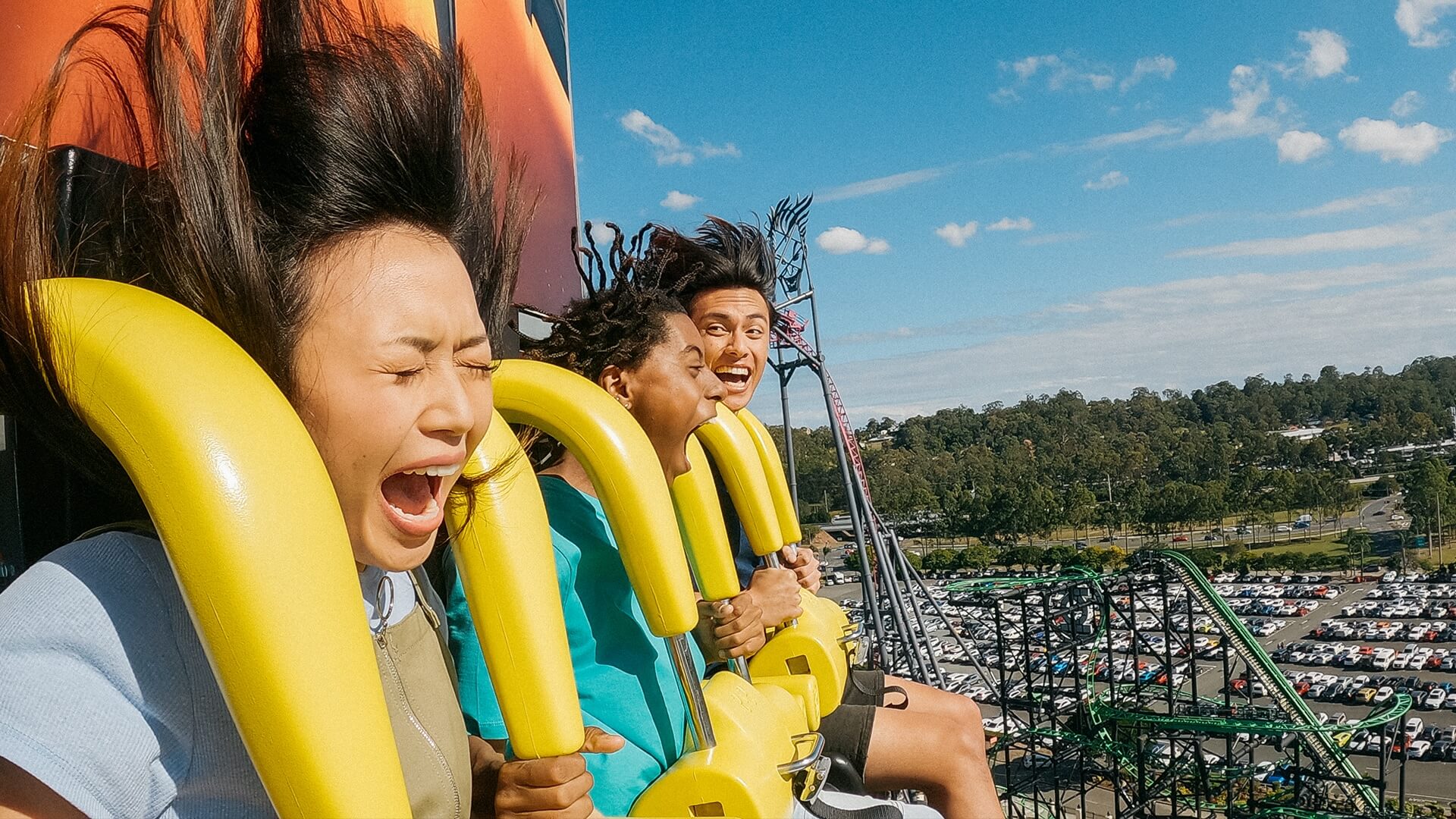 Excited riders experiencing BATWING Spaceshot, with a scenic view of the DC Rivals HyperCoaster and car park in the background at Warner Bros. Movie World, showcasing thrilling attractions and park surroundings