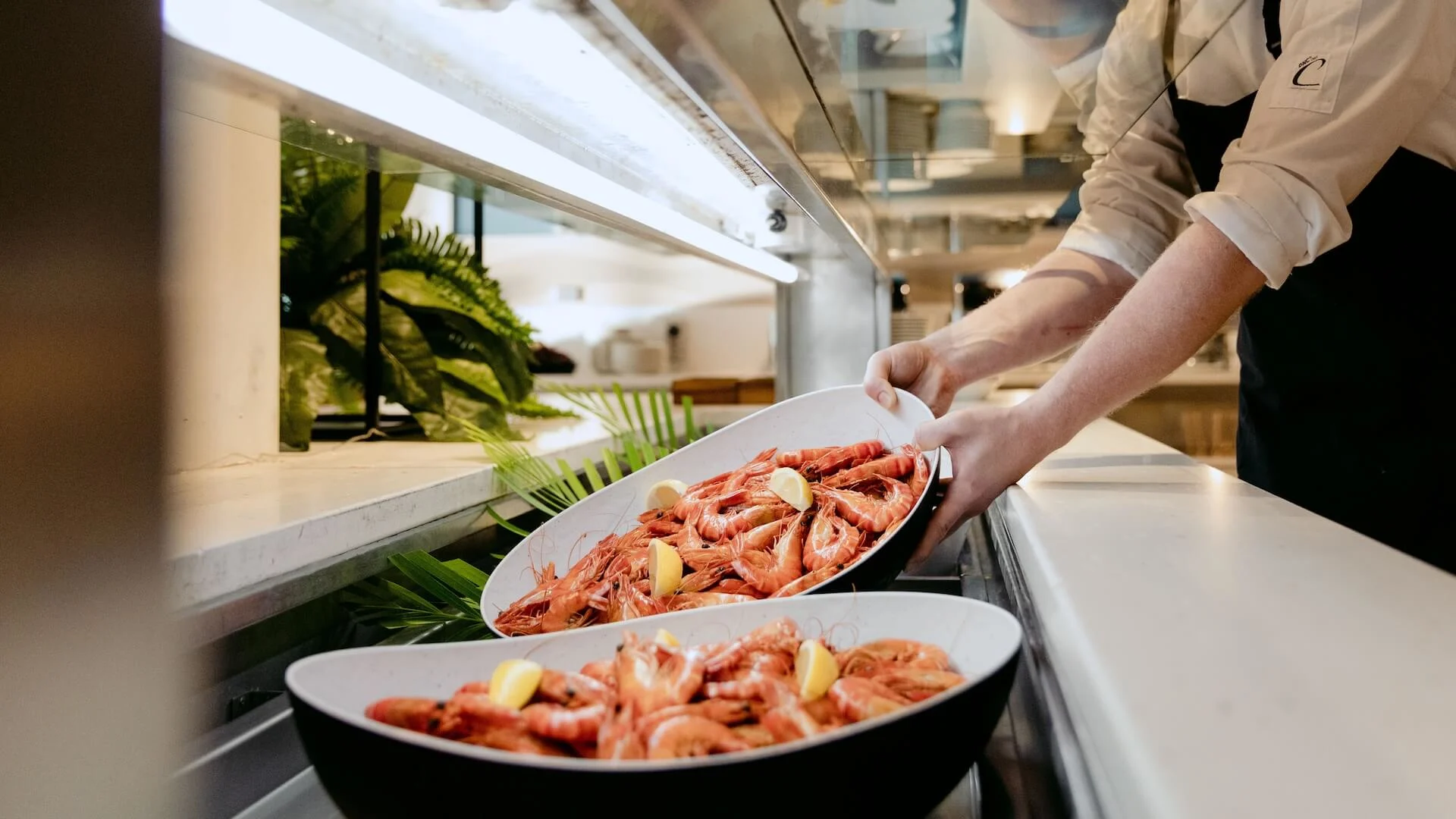 A chef arranges plates filled with shrimp and lemon slices on a countertop in Shoreline Restaurant for a seafood buffet.