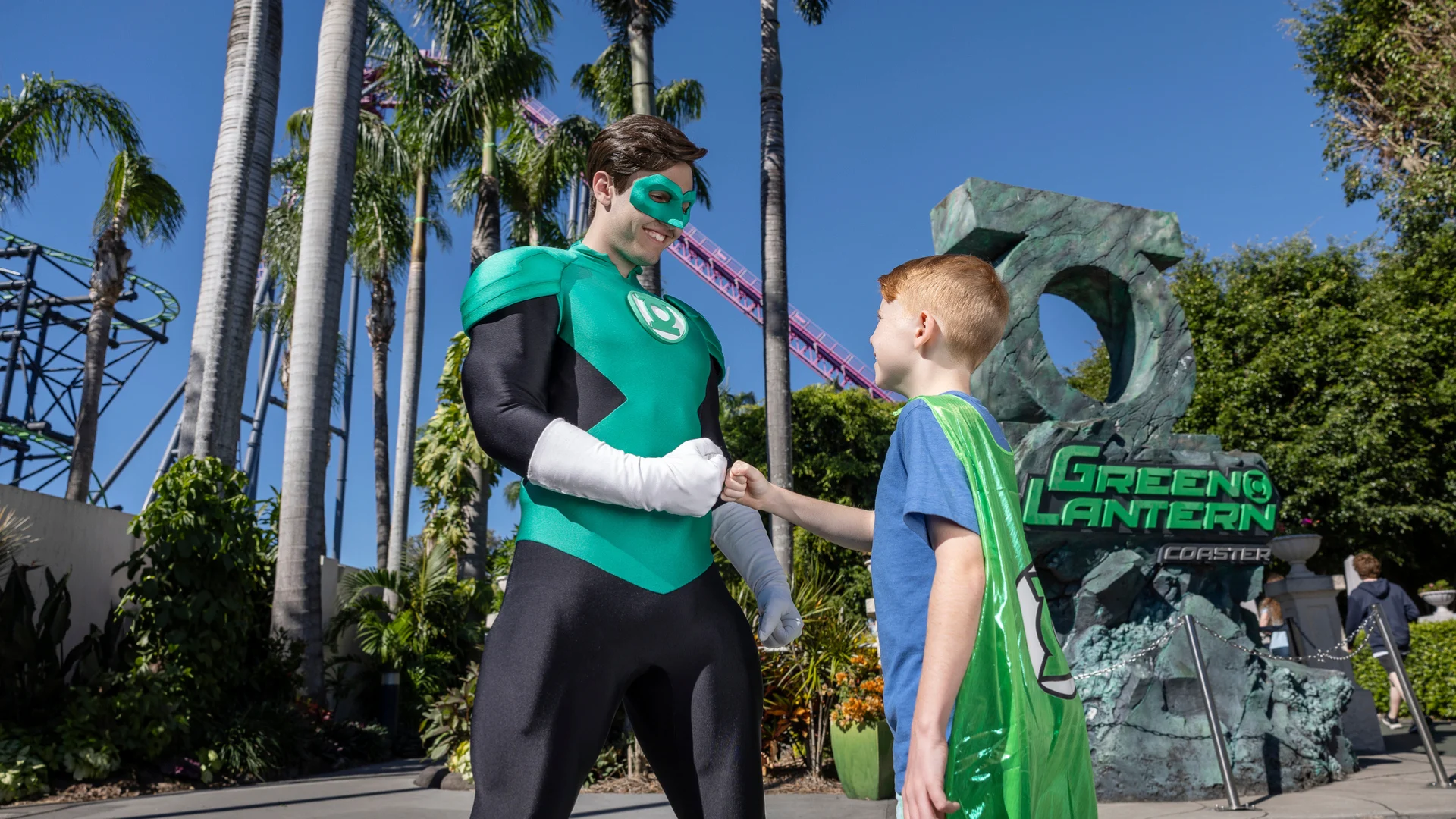 Green Lantern engaging in conversation with a young boy in front of the sign for Green Lantern Coaster at Warner Bros. Movie World