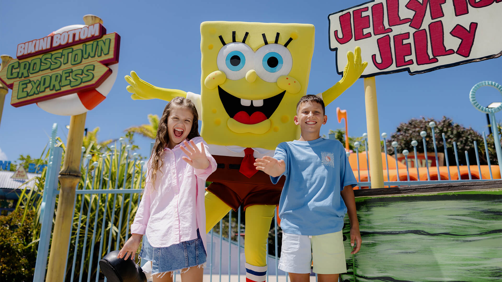 Two children grinning widely and waving with SpongeBob SquarePants, at Sea World on the Gold Coast.