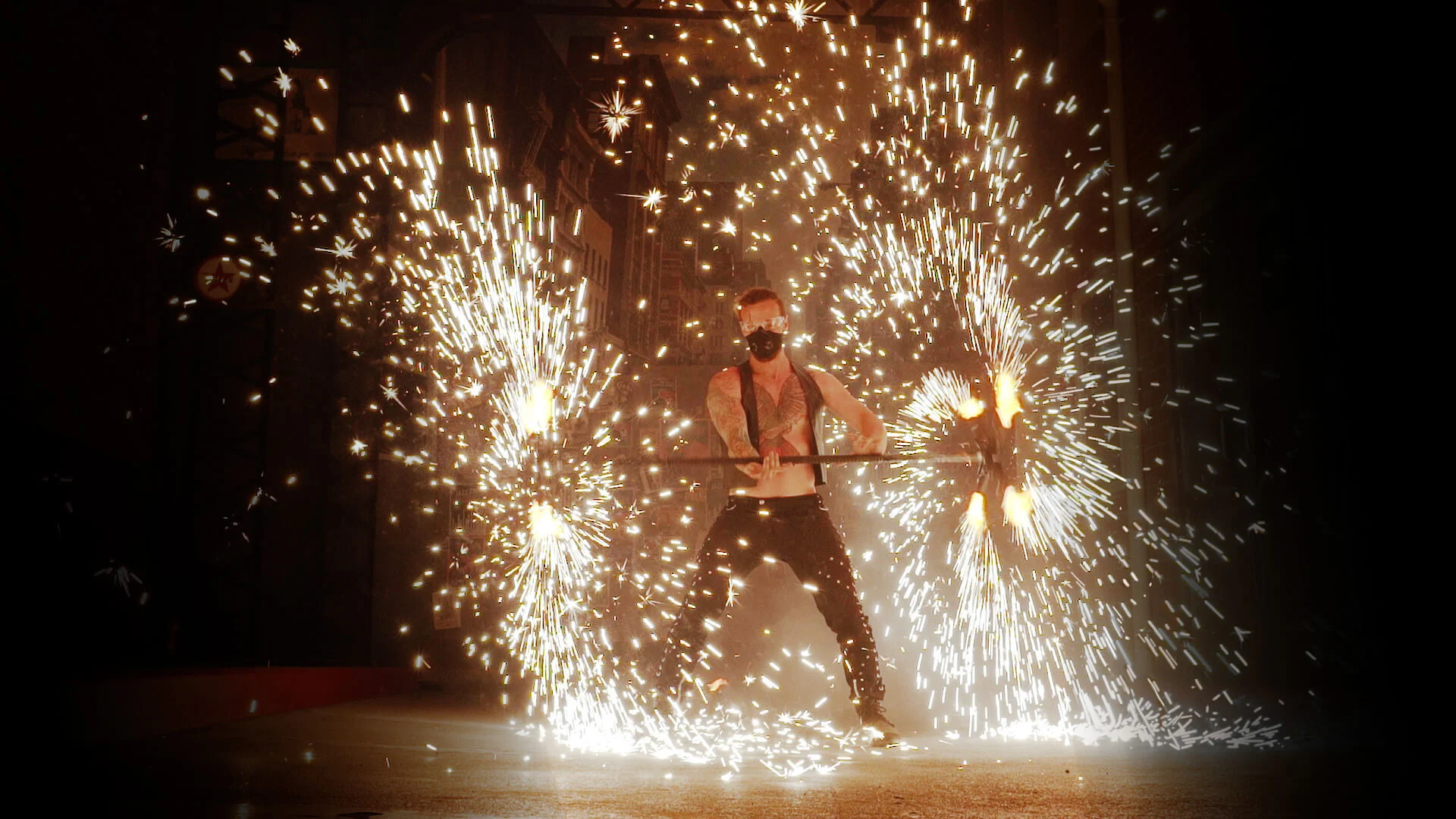 A performer wearing a mask spins a staff with sparks and fireworks radiating outward, creating a dramatic display of light and motion against a dark background.