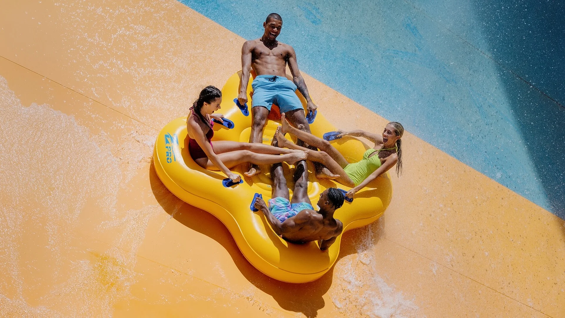 Group of friends riding together on a large yellow raft, sliding down Wet’n’Wild’s Tornado water slide with splashes and excitement.