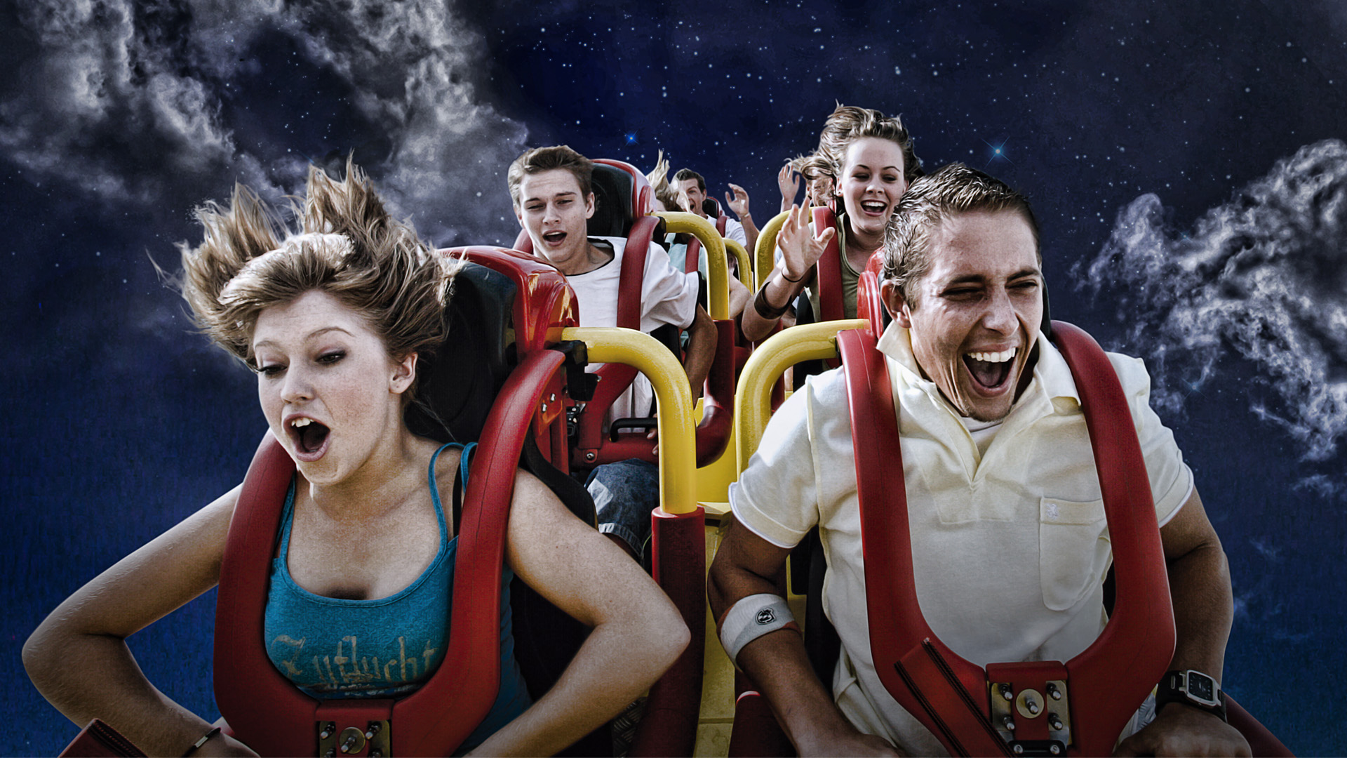 A group of young people ride a roller coaster at night, their faces showing excitement and fear as they speed down the track under a cloudy, moonlit sky.