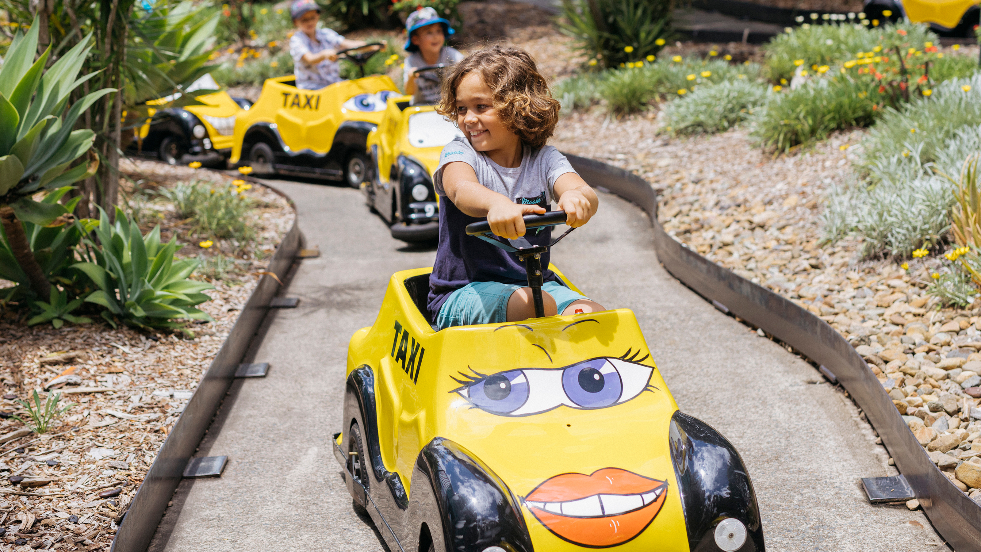 Children joyfully driving mini cars at Speedy Gonzales' Tijuana Taxis kids ride at Warner Bros. Movie World, having a fun and interactive experience in the theme park. Smiling