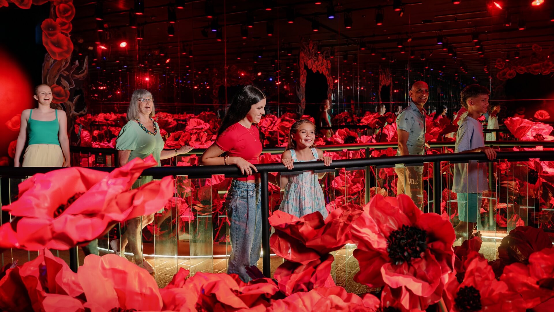 Visitors walking through the Wizard of Oz poppy field attraction at Movie World, surrounded by large red flowers and mirrored walls under red lighting