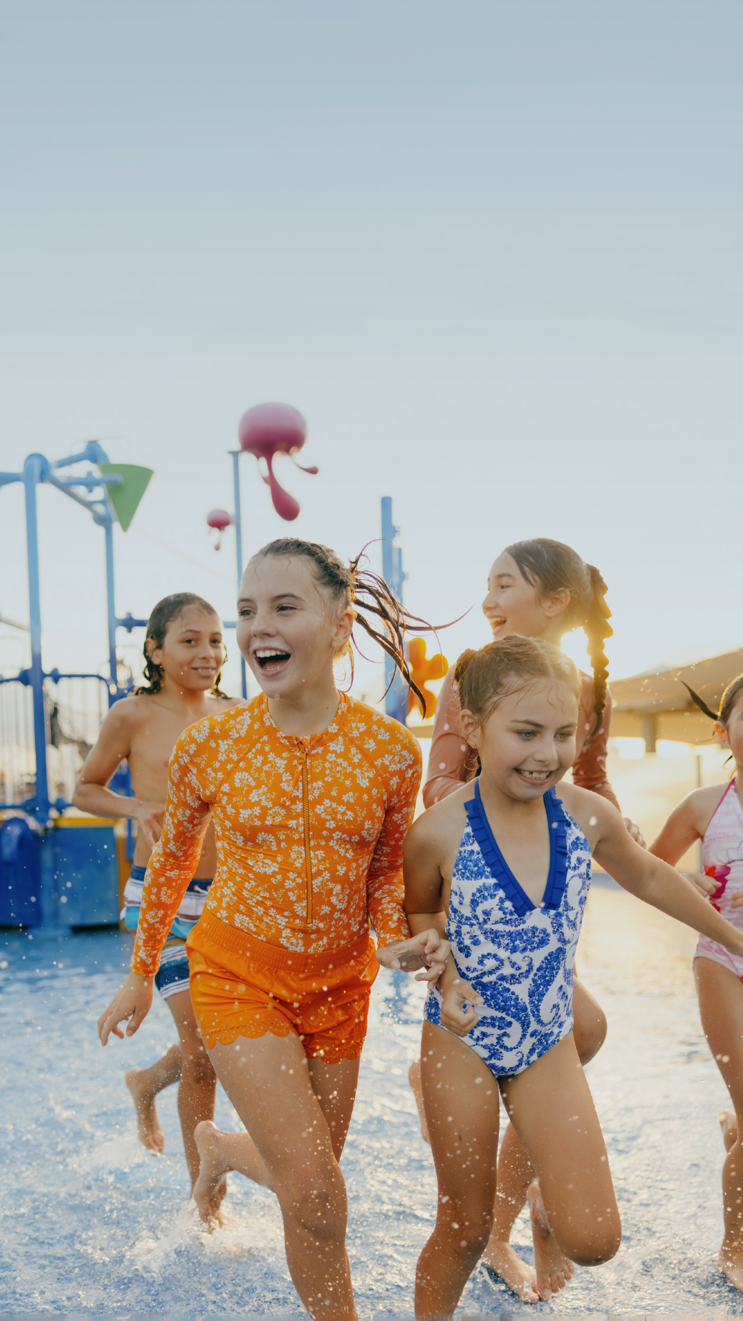 Children smiling and playing in a water park, wearing colorful swimsuits, with water splashing around them.