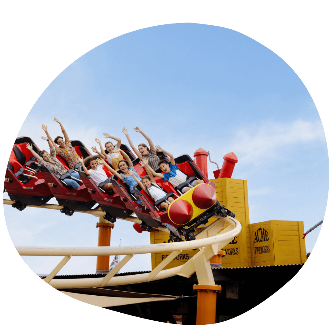 People riding a roller coaster at Warner Bros. Movie World with arms raised, against a clear blue sky.