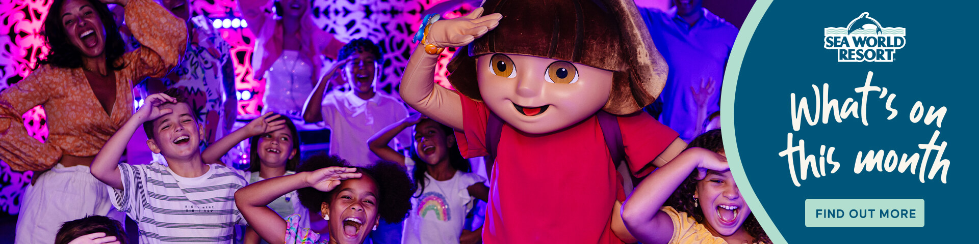 Children and adults pose and smile with a costumed character at an indoor Sea World Resort event, under colorful lighting.