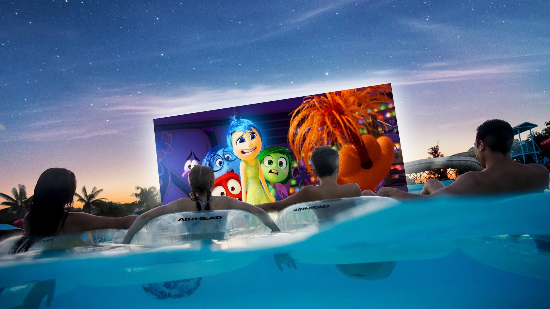 Families floating on pool tubes at Wet’n’Wild Dive-In Movies, watching an outdoor film under a starry night sky.
