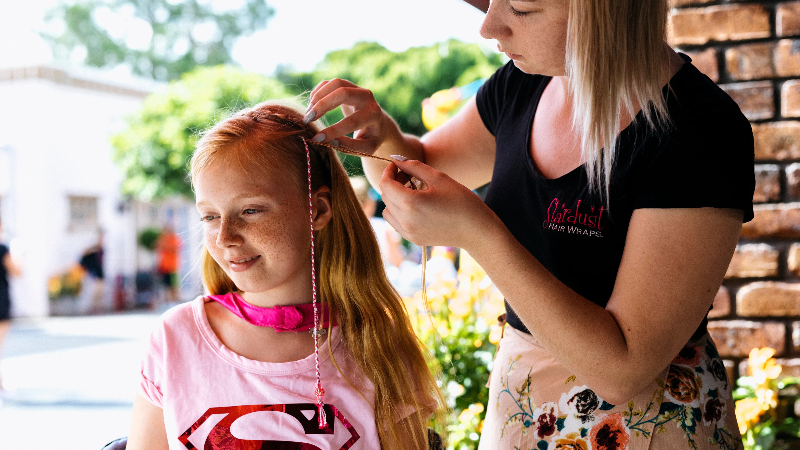A girl wearing superhero merchandise, getting her hair braided at Warner Bros. Movie World, adding a touch of fun and fantasy to her theme park experience