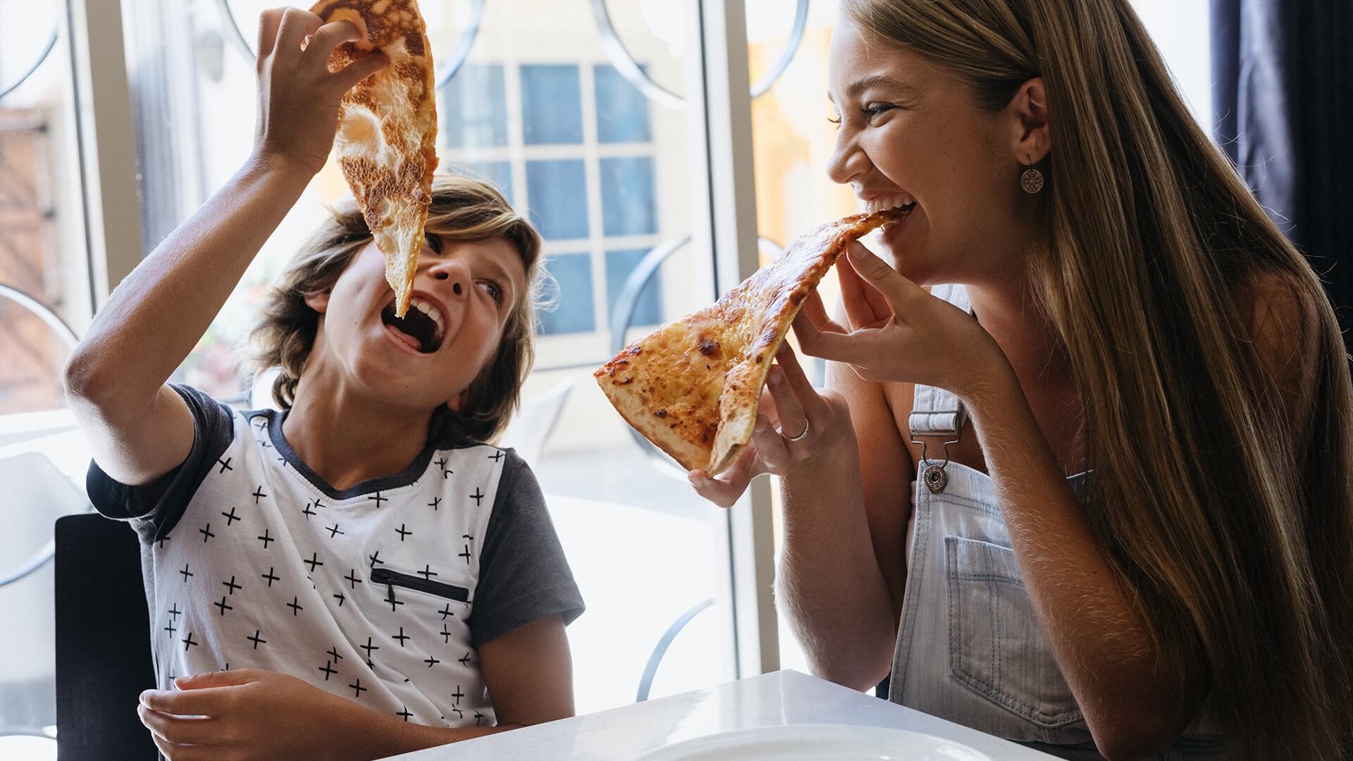 Two children happily eating pizza at Rick's Pizzeria at Warner Bros. Movie World, savoring delicious slices in a lively dining setting