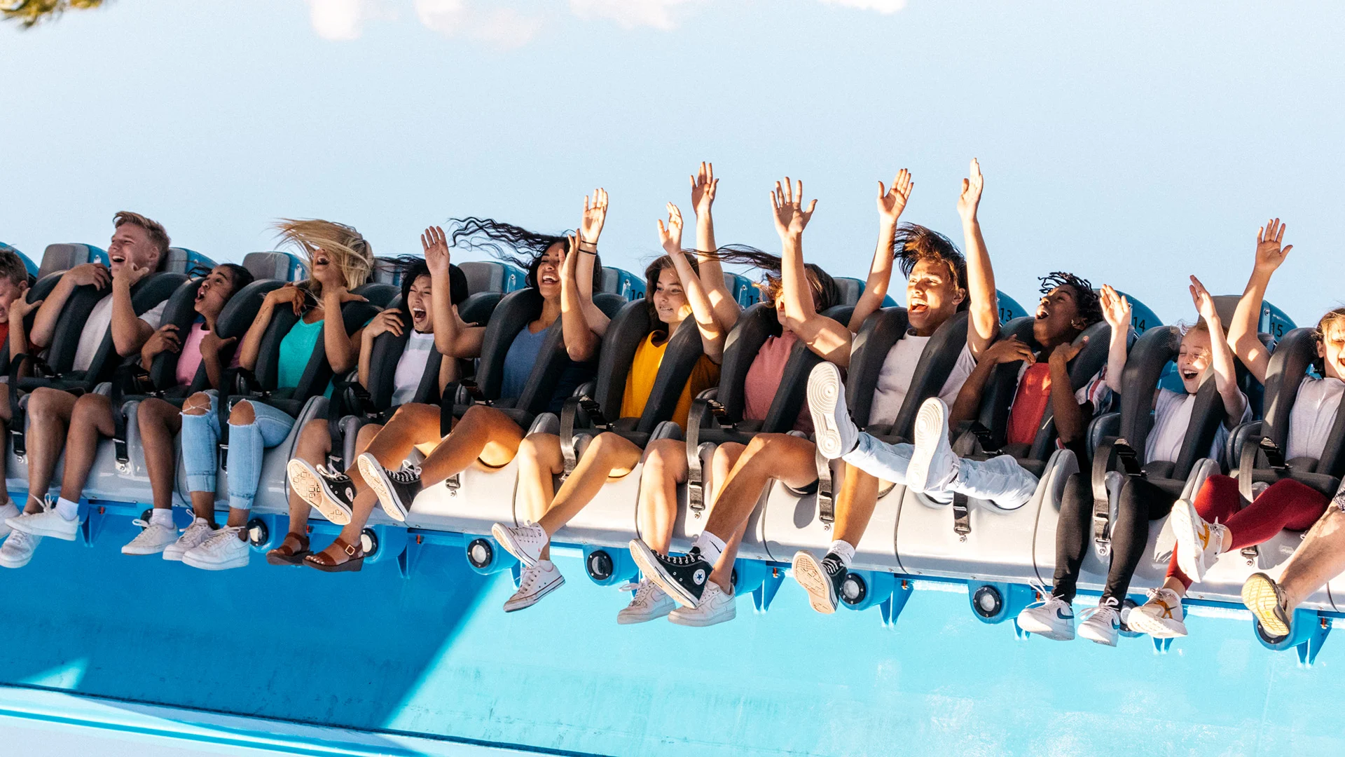 A group of people with raised arms ride an amusement park roller coaster, showing excitement and enjoyment under a clear sky.