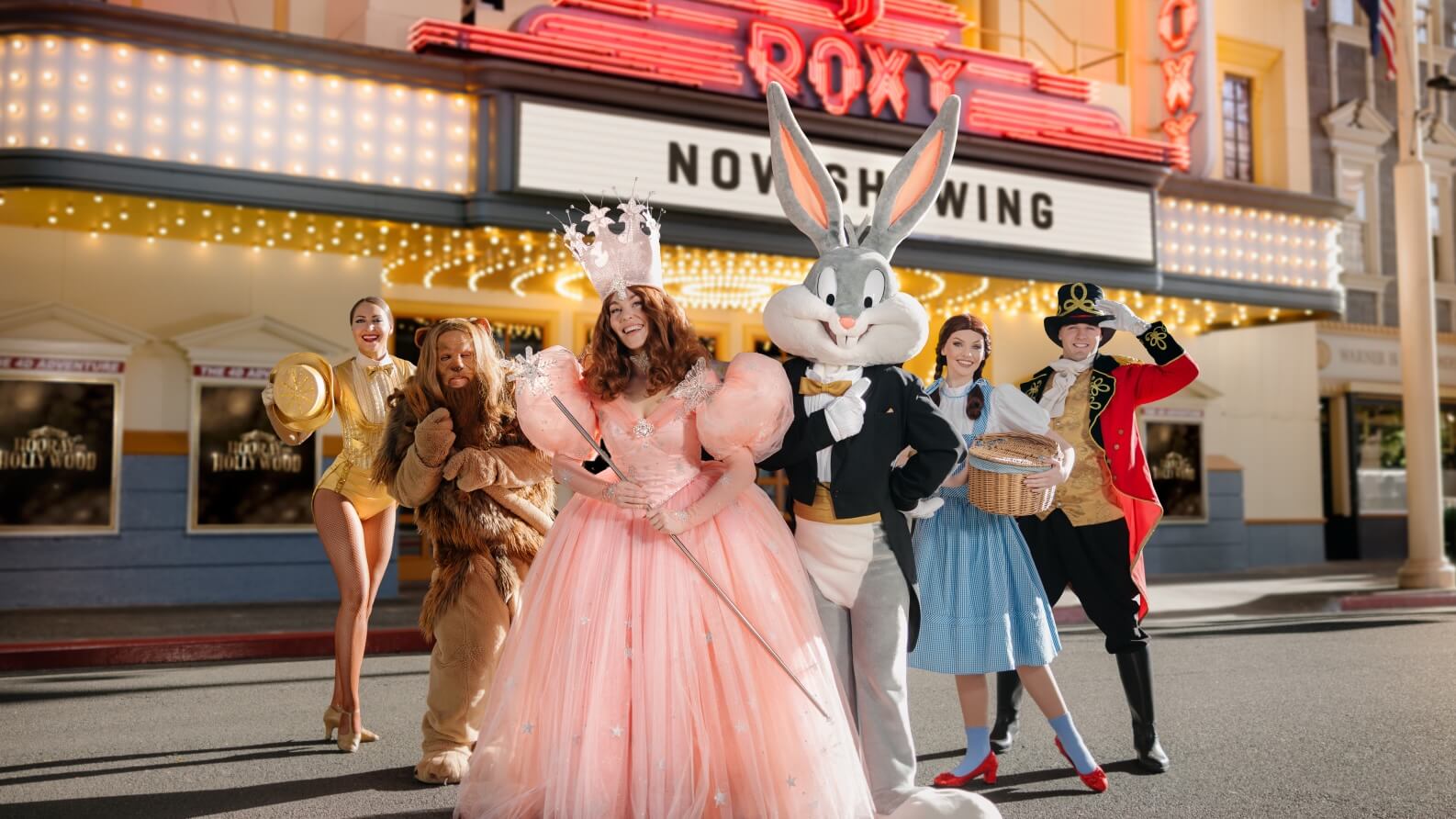 Costumed performers and Bugs Bunny posing in front of the Roxy Theatre at Movie World, dressed in Wizard of Oz-inspired outfits under bright marquee lights.