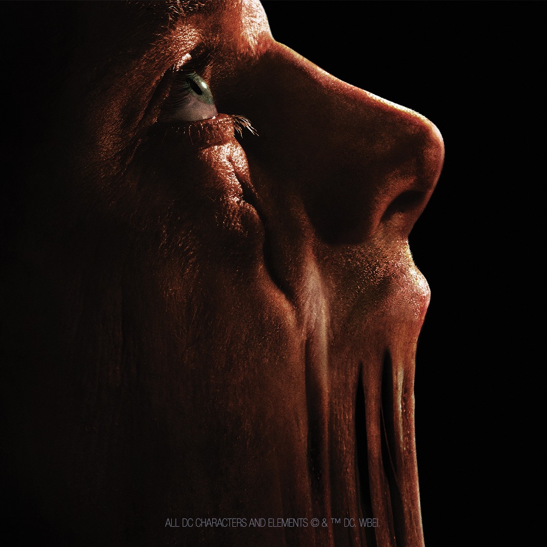 A close-up of a person’s face in profile, with skin stretched unnaturally down from the nose and mouth, creating a disturbing, melted appearance against a dark background.