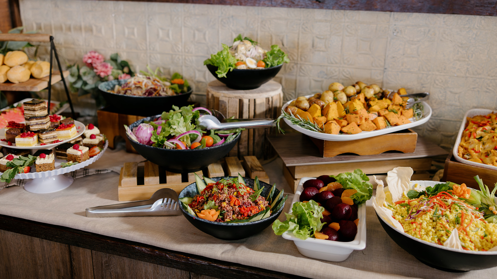 A buffet table with various salads, vegetables, bread rolls, and desserts arranged in bowls and trays, ready to be served.