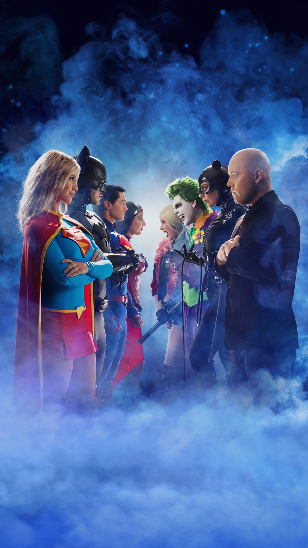 Two groups of costumed superheroes and villains face each other against a misty blue background, suggesting a confrontation. Characters include a woman in red and blue, a man in a bat suit, and a green-haired figure in clown makeup.