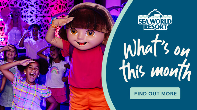 Children pose with a person in a Dora the Explorer costume at an event; Sea World Resort sign promotes monthly activities.
