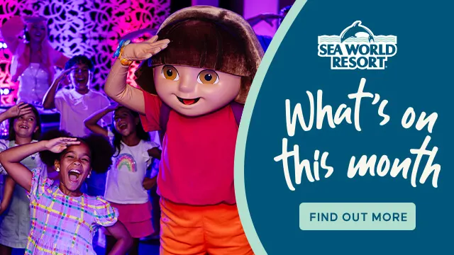 Children pose with a person in a Dora the Explorer costume at an event; Sea World Resort sign promotes monthly activities.