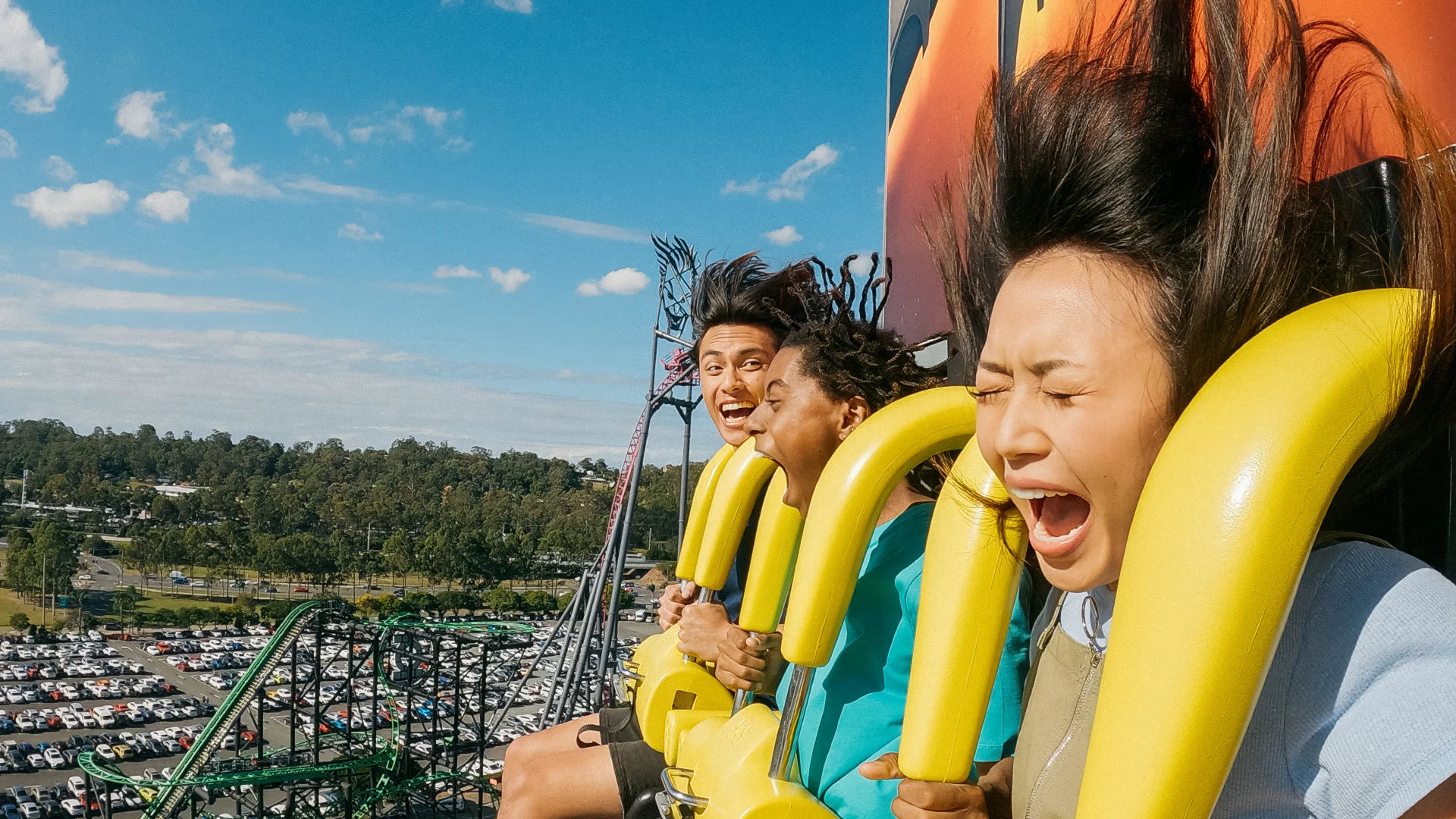 Excited riders experiencing BATWING Spaceshot, with a scenic view of the DC Rivals HyperCoaster and car park in the background at Warner Bros. Movie World, showcasing thrilling attractions and park surroundings