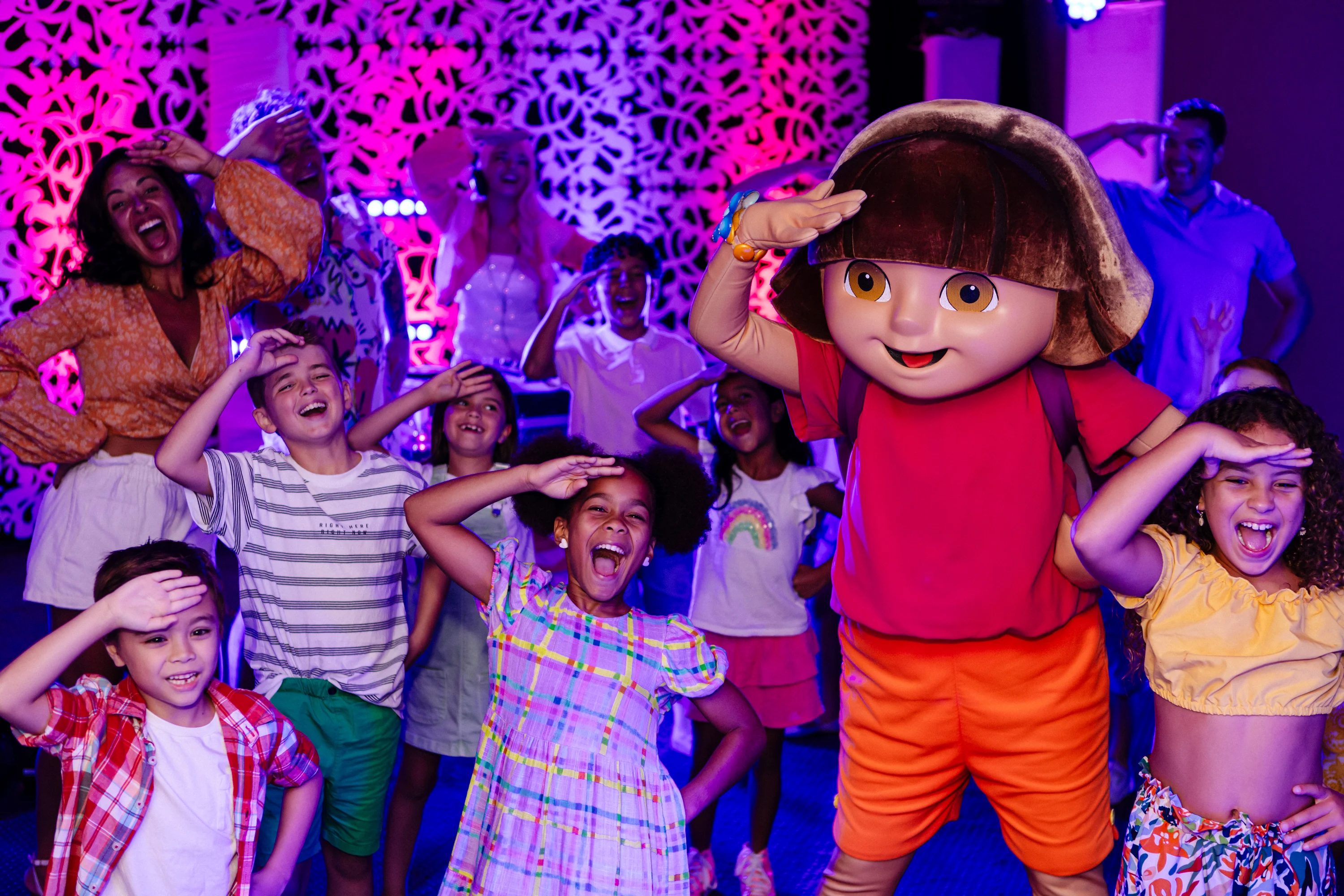 A group of children and adults smile and pose while a large cartoon character in a red shirt stands in front of them.