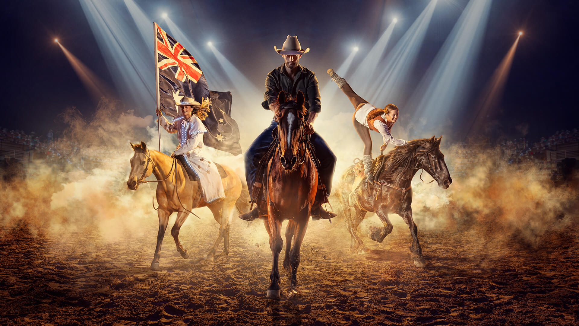 Three horseback riders perform under spotlights in a dusty arena. One rider holds an Australian flag, another does a handstand on a horse, and a central rider wears a cowboy hat.
