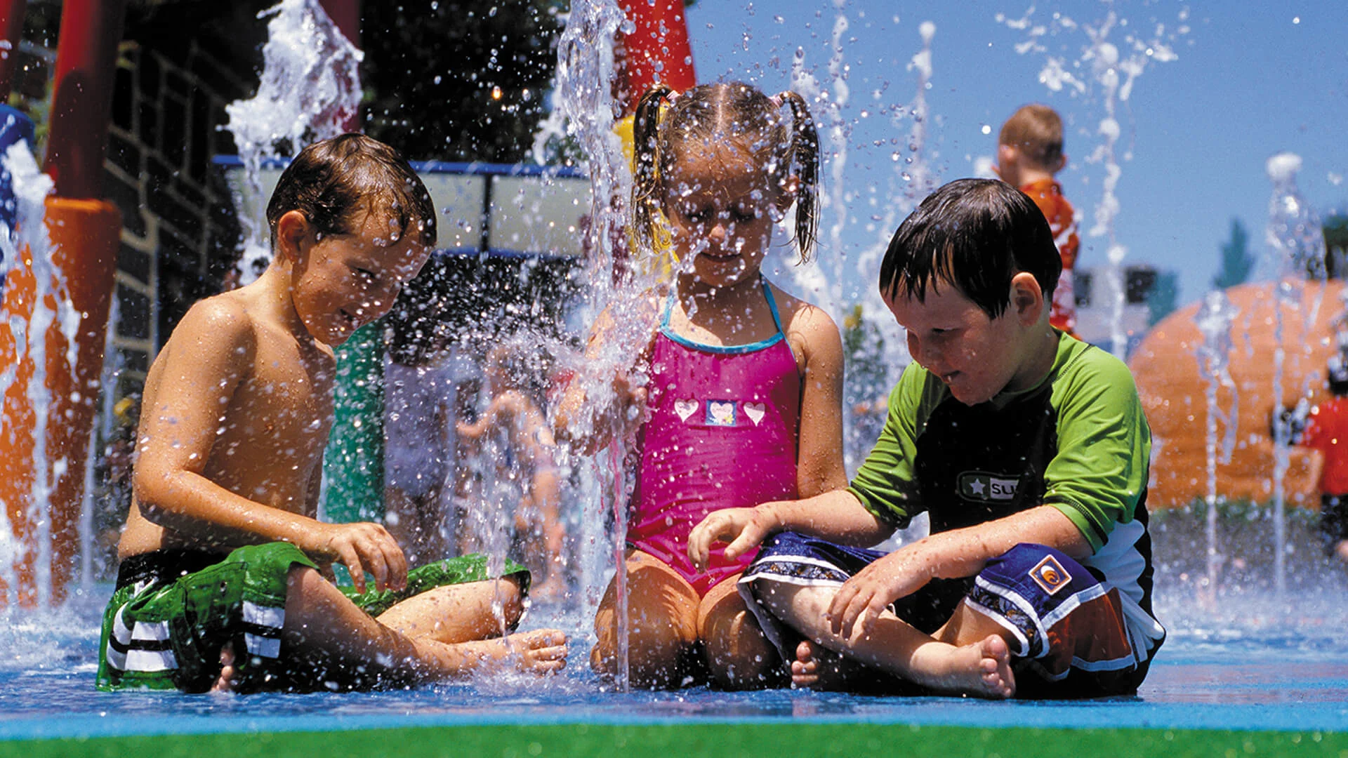 Three children playing and splashing in the water feature at the Looney Tunes Splash Pad at Warner Bros. Movie World
