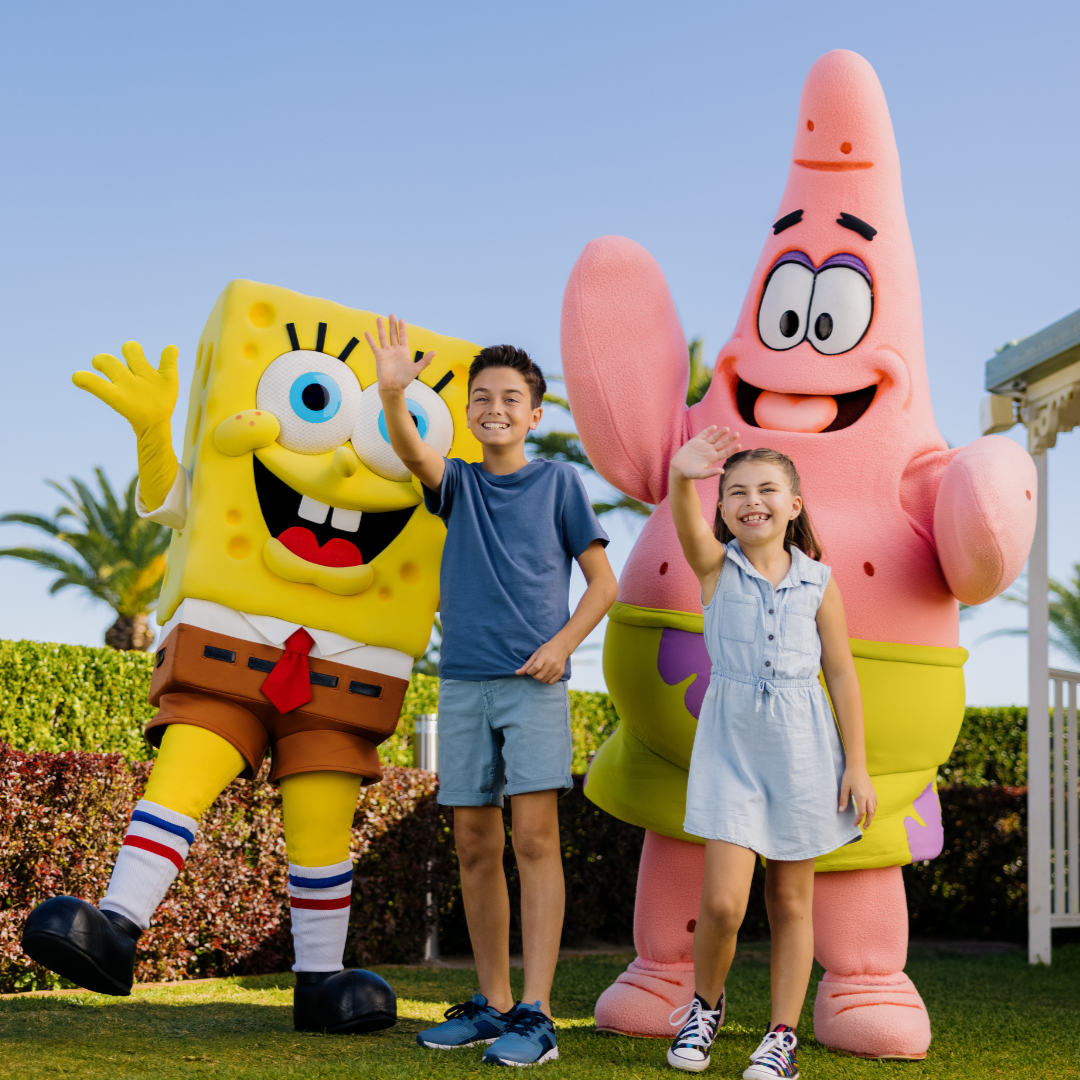 Two kids smile and wave alongside SpongeBob SquarePants and Patrick Star in an outdoor setting at Sea World Resort.