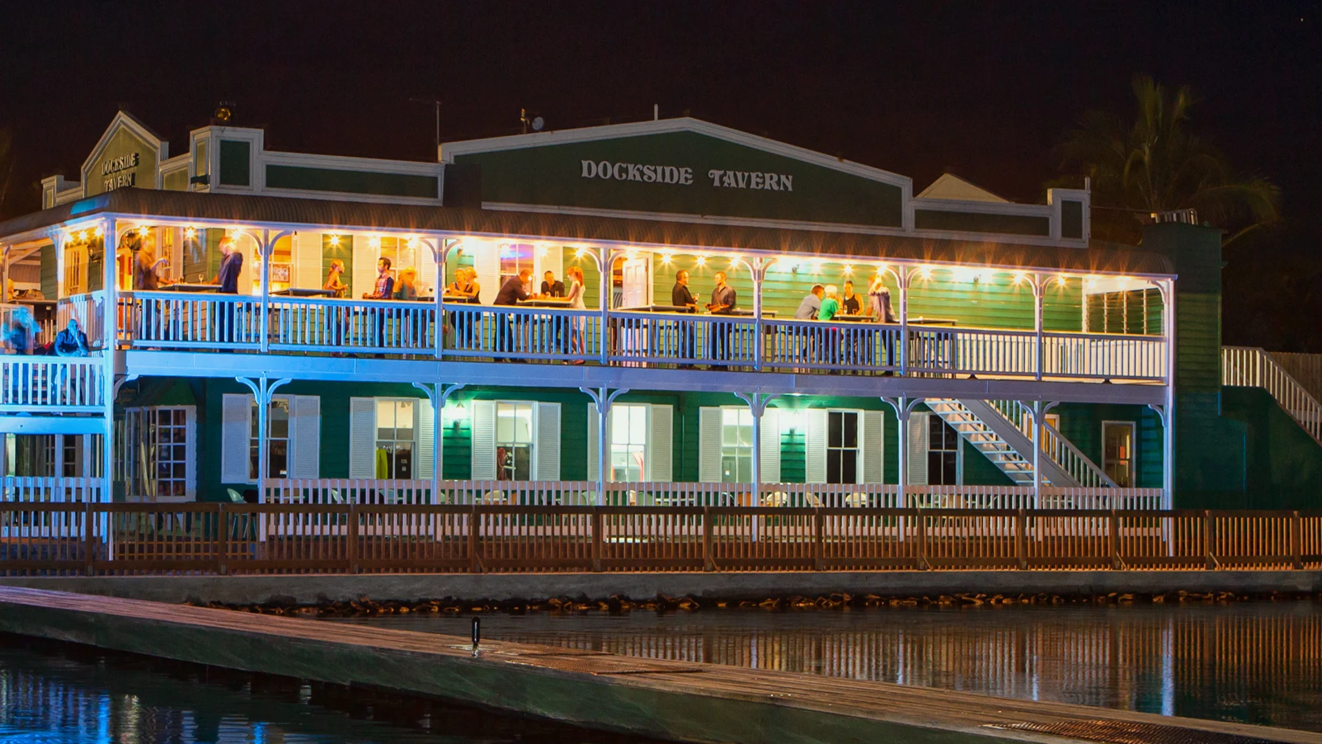 A two-story building labeled "Dockside Tavern" is lit up at night, with people on the upper balcony and a dock in the foreground.